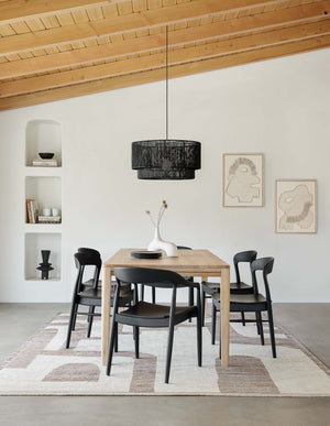 The Abode geometric two-toned kand-knotted floor rug by Élan Byrd with woven border sits in a dining room with black ida dining chairs, a black jute chandelier, and a sloped wooden beamed ceiling