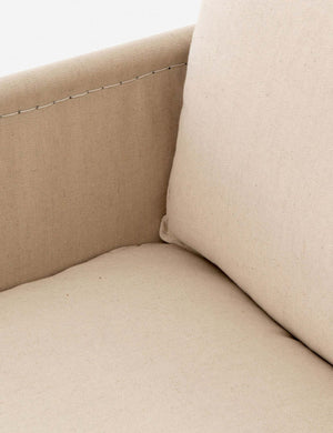 Close-up of the cream linen cushioning and stitch work on the arm from the inside of the Alena accent chair with black metal frame