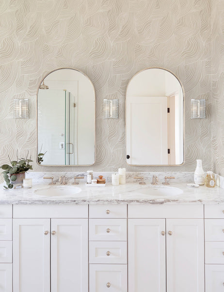 #color::neutral | Alina neutral Wallpaper with smooth ripple pattern is in a bathroom with white countertops and cabinetry and two arched mirrors