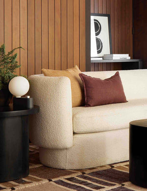 The arlo aubergine lumbar pillow sits in a retro room on a cream boucle sofa