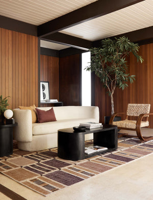 The Anni rug lays in a retro living room with wood-paneled walls under a cream boucle sofa and black oval coffee table