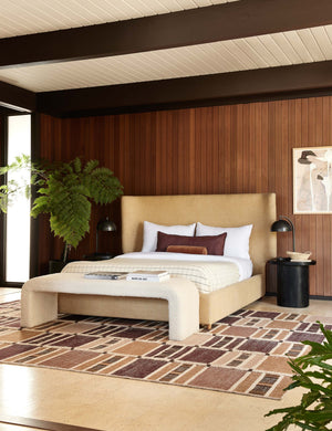 The Luna black wood round side table sits next to a camel linen framed bed and a red, orange, and natural patterned rug