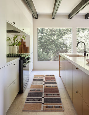 The Anni runner rug lays in a kitchen with white cabinetry, black beamed ceilings, and large square windows
