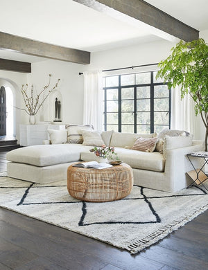 The aya moroccan shag rug lays in a living room with black beamed ceilings under a linen sectional