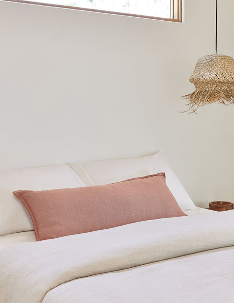 #color::terracotta #style::long-lumbar | The arlo Terracotta long lumbar pillow lays on a bed with ivory linens with a jute pendant light hanging next to it