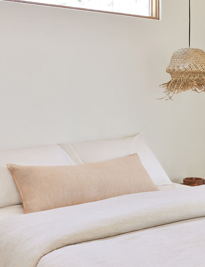 #color::blush #style::long-lumbar | The arlo Blush pink long lumbar pillow lays on a bed with ivory linens with a jute pendant light hanging next to it