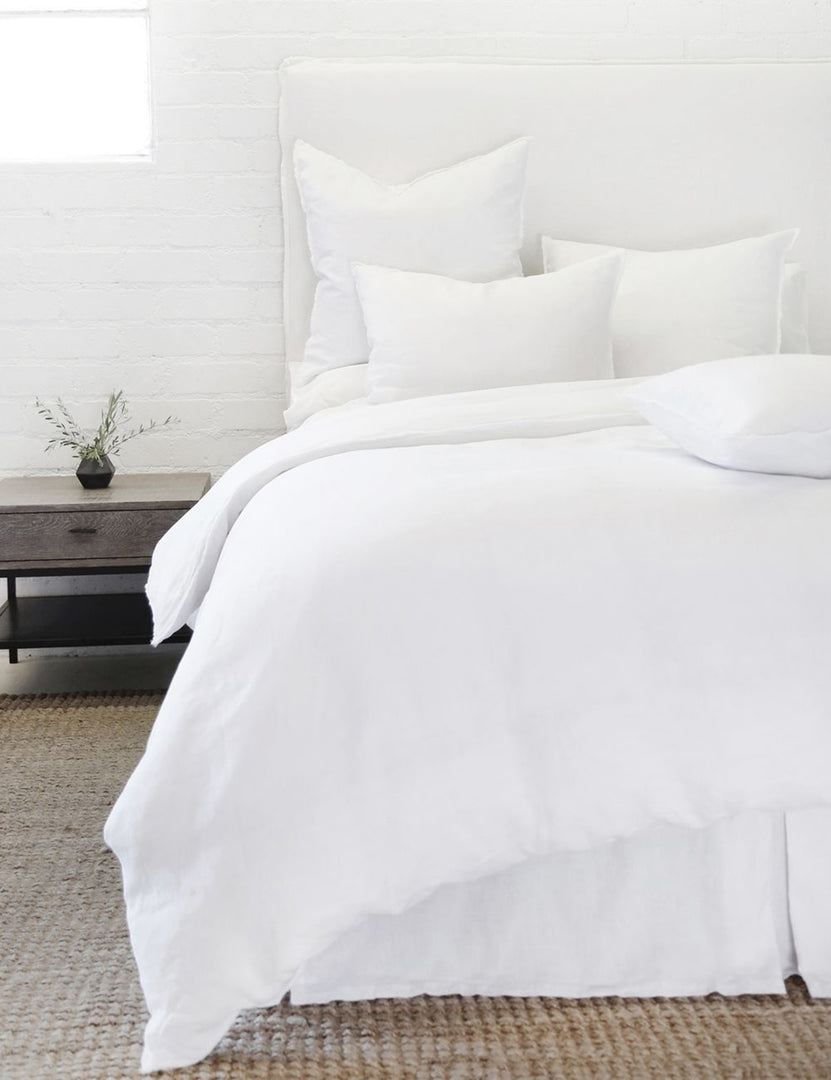 #color::white #size::king #size::queen | The white blair stonewashed linen duvet by pom pom at home lays atop a white linen framed bed in a bedroom with a jute area rug, a white brick wall, and a wooden nightstand