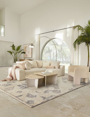 The Giles Moroccan Shag Rug lays in a white-toned room under two nested coffee tables, an ivory linen sofa, and an accent chair