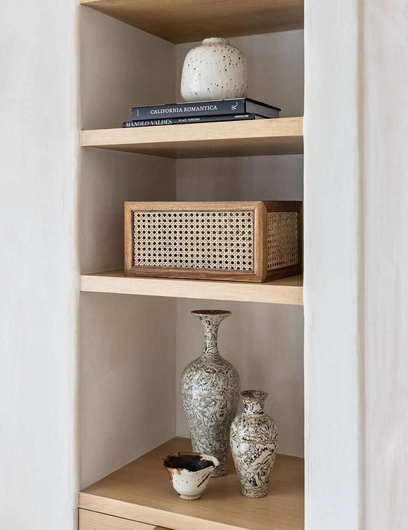 | Rattan cane bin by NEAT Method sits on a shelf with a book and various vases
