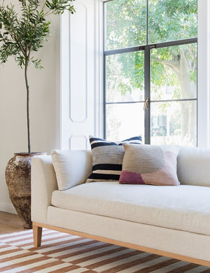 The Charleston Ivory Linen sofa sits against a bright window atop an ochre and white striped carpet