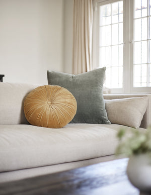 The Monroe mustard yellow velvet round pillow sits on a natural sofa with a shale blue velvet throw pillow