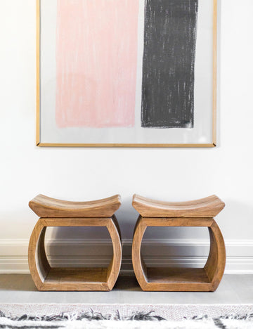 | Two devlin stools sit next to each other underneath a pink and black wall art