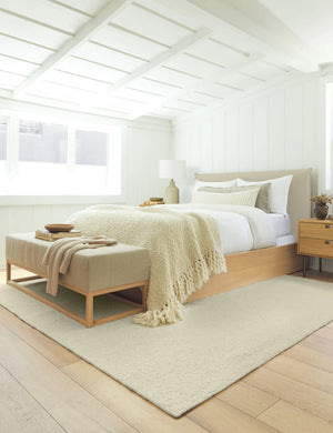 The dune rug lays in a bedroom with sloped ceilings under a neutral linen bench and a wooden and linen framed bed