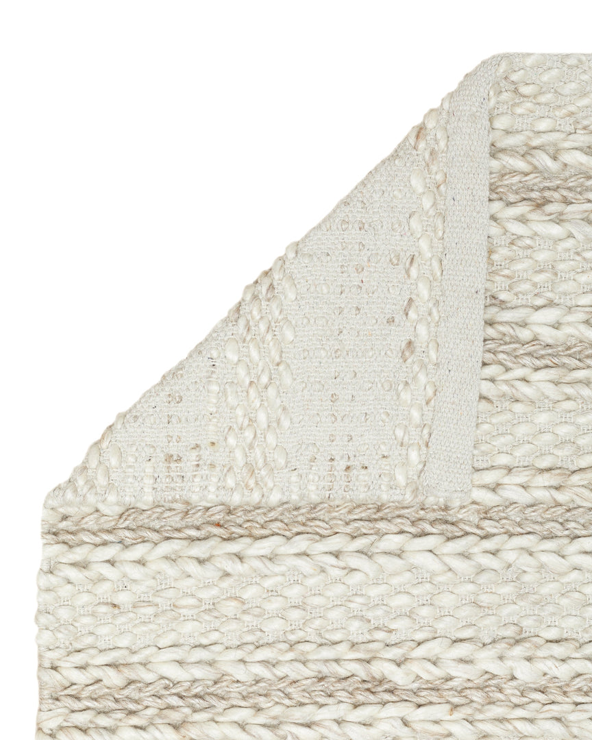 #size::3--x-5- #size::5--x-8- #size::8--x-10- #size::9--x-12- #color::soft-sand #size::10--x-14- | Close-up of the corner of the Estie white rug with thick braids slightly folded over, exposing the underside of the rug | The corner of the Estie rug folded over itself