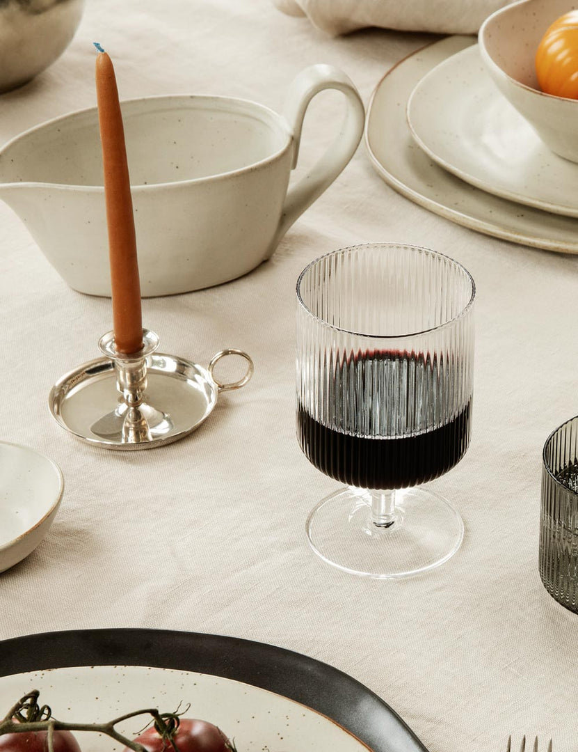 | One rian ripple wine glass sits atop a dining room table with a terracotta taper candle and a white gravy boat