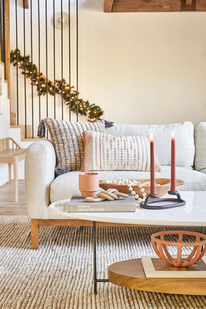 The Prong terracotta ceramic centerpiece bowl by SIN sits beneath the thomas bina olivia oval coffee table in a festive living room with a gray linen sofa and a woven rug