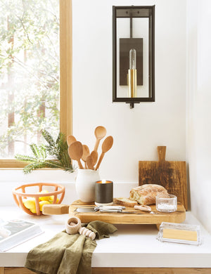 The Prong terracotta ceramic centerpiece bowl by SIN sits on a white countertop in a kitchen with wooden cutting and cheese boards, olive green linens, and a black sconce light with golden hardware