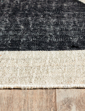 Close-up of the black semi-circle and neutral toned fabric on the Goubi flatweave area Rug by Lemieux et Cie x Momeni