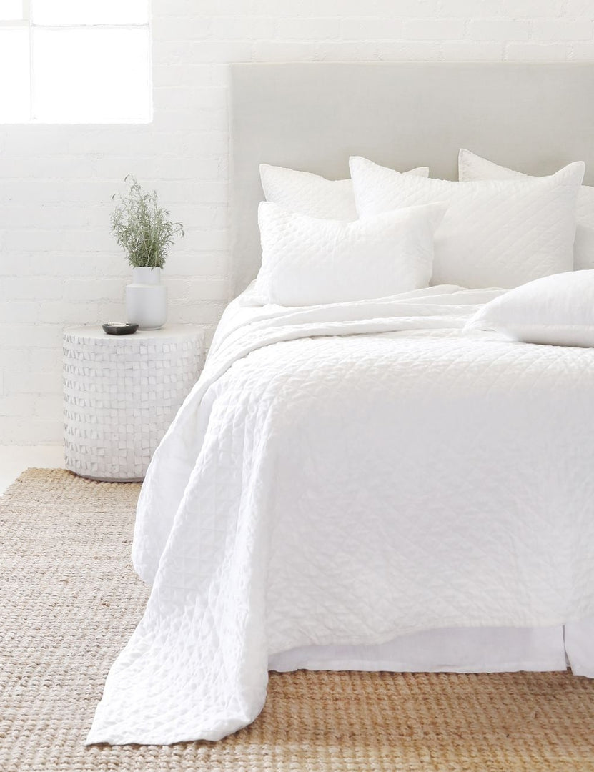 #color::white #size::king #size::queen #size::twin | The Hampton white Quilted Coverlet by Pom Pom at Home lays on a white linen framed bed in a bedroom with a jute rug and a white brick wall