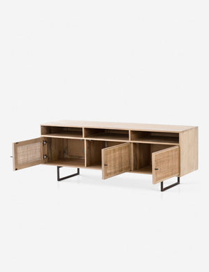 Angled view of the Hannah natural mango wood media console with its three cane doors open, revealing the inner shelving.
