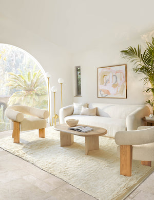 The Celeste honey wood accent chair with wishbone frame sits in a bright living room with a natural wood coffee table, natural linen sofa, and plush white rug.