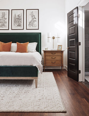 The helene rug lays under an emerald green framed bed in a bedroom with three nature-inspired paintings and a wooden nightstand