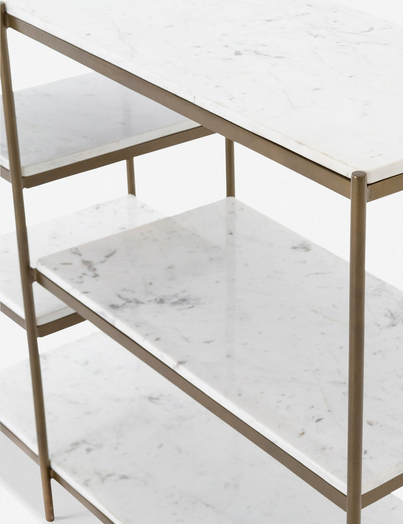 | Angled close-up of the shelving on the right side of the Kathleen console table with marble shelves and gold finish