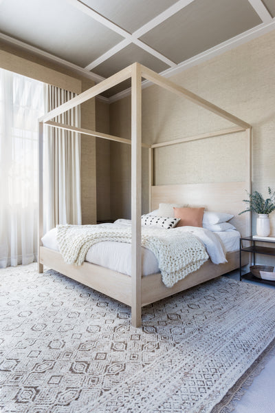 #color::white-swan | The Sable white swan ultra-chunky throw blanket by Nikki Chu lays in a bedroom at the edge of a white-washed wooden canopy bed that sits atop a textured white and brown carpet