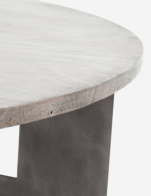 Close-up of the side of the light mango top and top of the iron leg on the base of the Andra round coffee table with light mango wood top and iron X-base Andra round coffee table