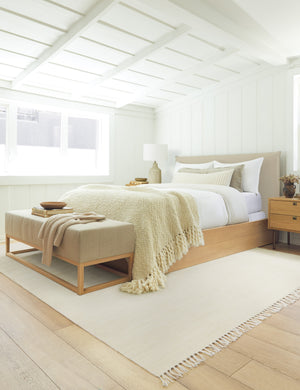 The Sierra Rug lays in a bedroom under a neutral and wooden framed bed, a wooden nightstand, and a neutral bench