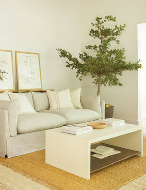 The Aprilette Coffee Table sits in a living room with a jute rug, two wall arts, and a natural linen sofa
