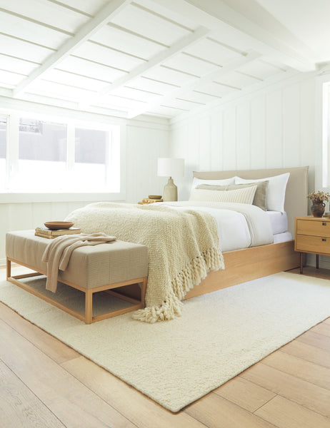 #size::cal-king #size::king #color::natural #size::queen | The Nia natural linen bed sits atop an ivory rug with a linen bench under a white sloped ceiling