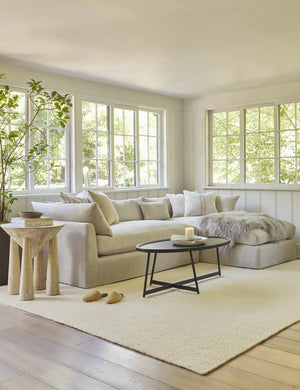 The dune rug lays in a living room with wrap-around windows under a sectional sofa and oval coffee table