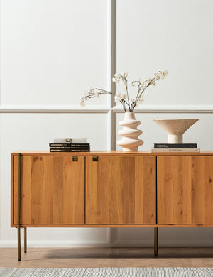 The Karma Sideboard sits in front of an accented wall with a sculptural vase, centerpiece bowl, and stack of books atop it