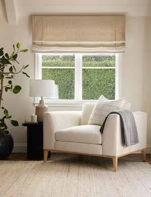 The Charleston ivory linen accent chair sits in front of a window atop a natural-toned rug next to a black side table