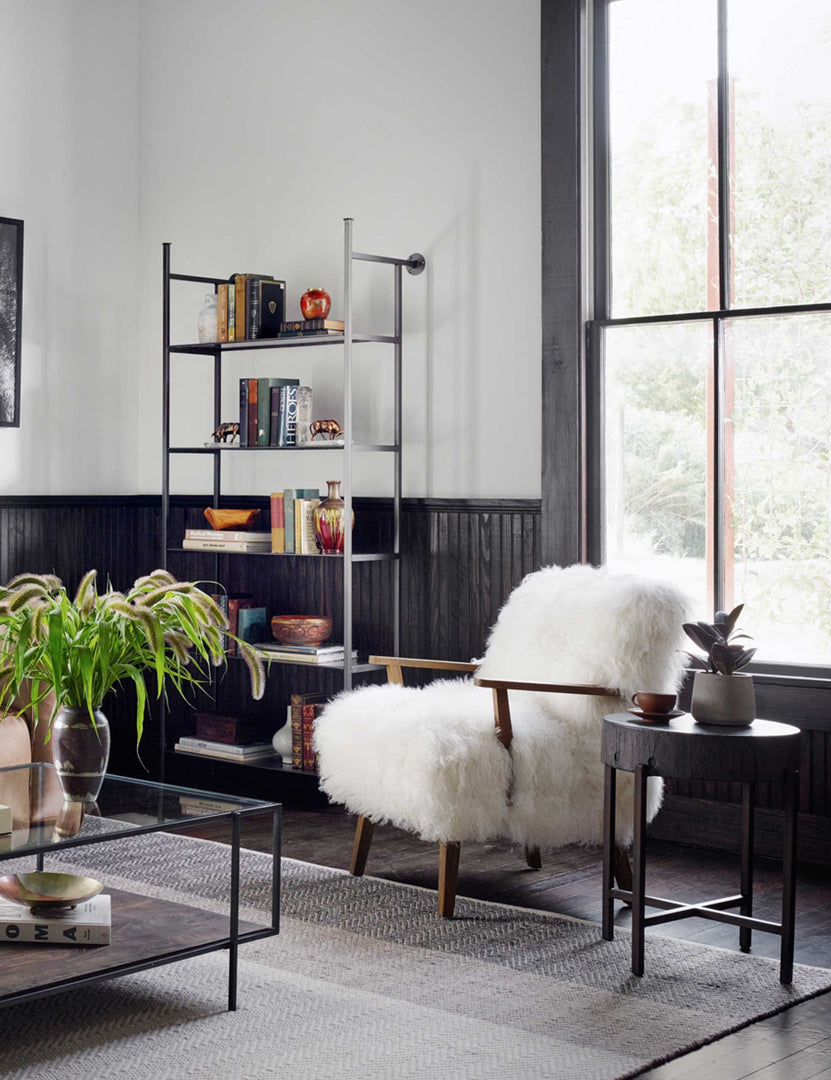 | The Kora accent chair sits in a living room with black paneled walls, a gray-toned rug, and a black side table