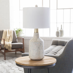 The Langley table lamp with stone base and white finial sits in a living room atop a wooden side table with a gray accent chair and sofa in the background