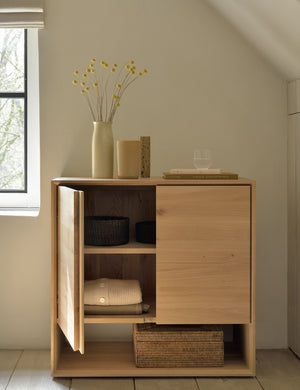 The Lark 2-Door Sideboard with one door open sits in an attic space with a vase and book atop it
