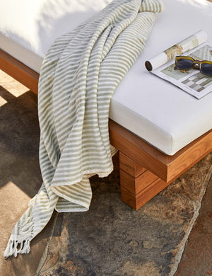 Sage green and white striped Beach Towel by Business & Pleasure Co hangs off a white cushioned outdoor lounge chair