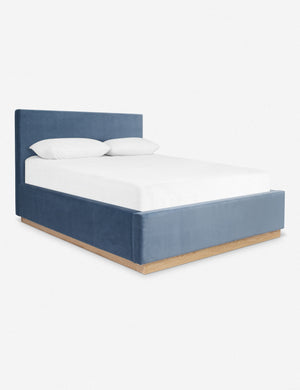 An angled side view of the Lockwood blue velvet-upholstered bed with a white oak base.