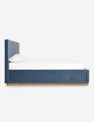 A side view of the Lockwood blue velvet-upholstered bed with a white oak base.