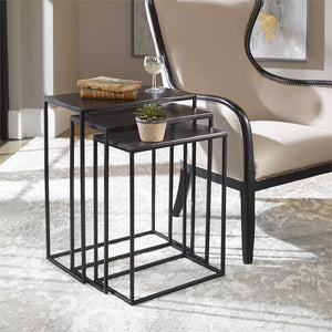 The Loletta black nesting tables are partially nested under each other, sitting in a living room next to a black wooden framed accent chair atop a gray patterned rug
