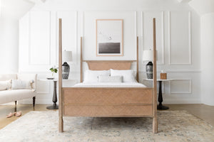 The Auriel side table with marble table top and cast iron base sits in a bedroom on both sides of a woven cane bed against a white accented wall