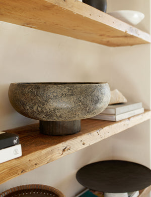 Close-up of the Lakshmi terracotta bowl with antiqued black finish and woven base sitting on a wooden shelf with other centerpiece decor and stacks of books
