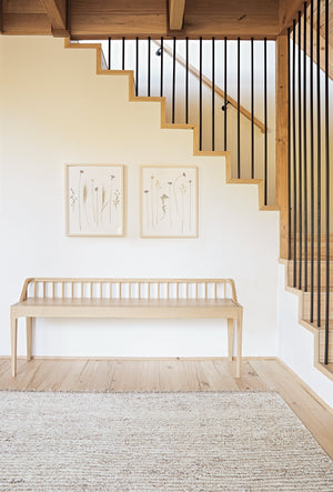 The Kenzi sand rug lays in front of a staircase next to a wooden bench and two wall arts