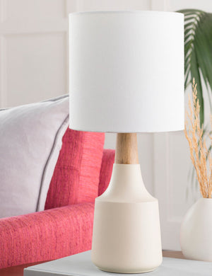 The Marcella cream vase-shaped Mini Table Lamp with ceramic base sits in a living room atop a white side table next to a bright pink sofa
