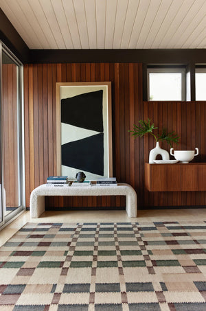 The marli rug lays in a retro room with wood-paneled wall, a geometric wall art, and a cream boucle bench