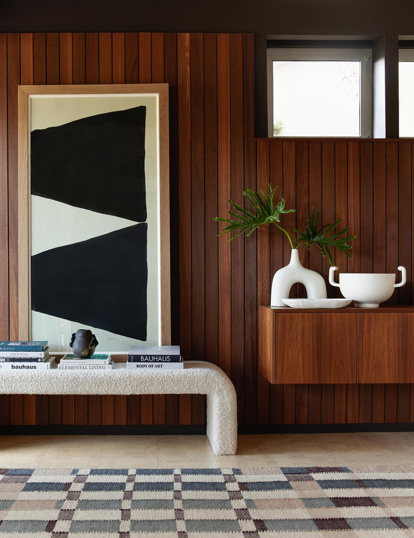 | The Sculpture II geometric two-toned print sits in a retro space against a wood paneled wall above a white boucle bench and a multicolored patterned rug.
