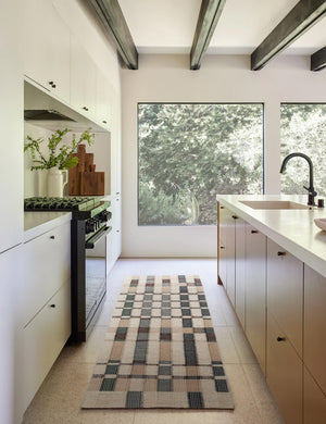 The marli rug in its runner size lays in a kitchen with white cabinetry, black beamed ceilings, and large square windows
