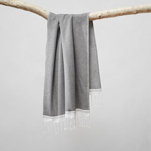 The Mediterranean Turkish Cotton gray Guest Towel by Coyuchi with tasseled ends hangs off a branch